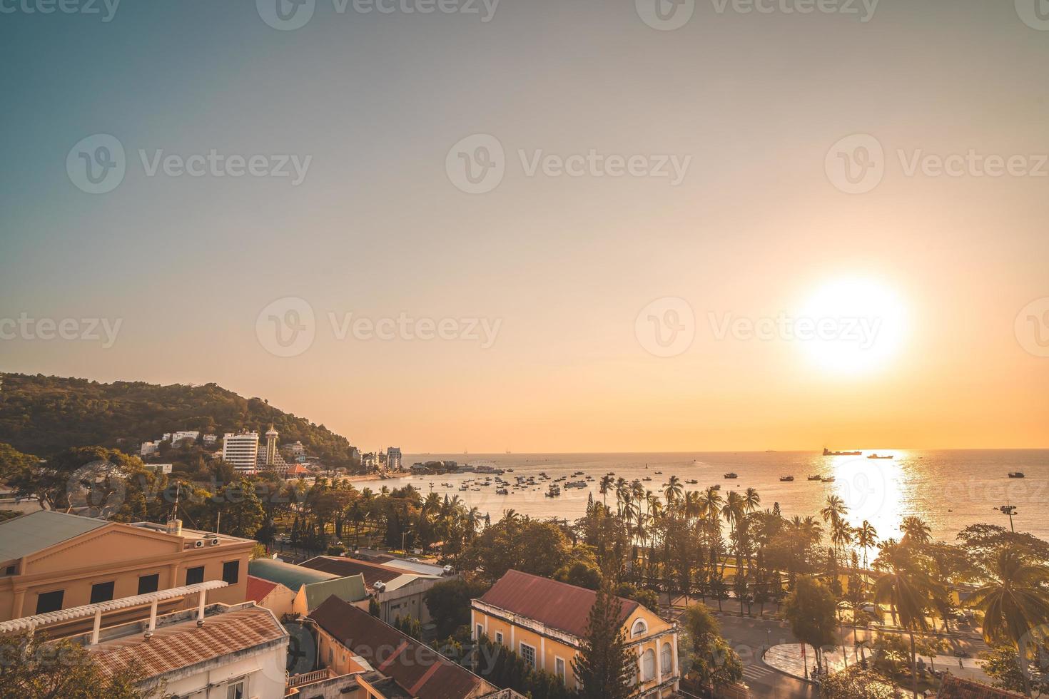 Vung Tau city aerial view with beautiful sunset and so many boats. Panoramic coastal Vung Tau view from above, with waves, coastline, streets, coconut trees and Tao Phung mountain in Vietnam. photo