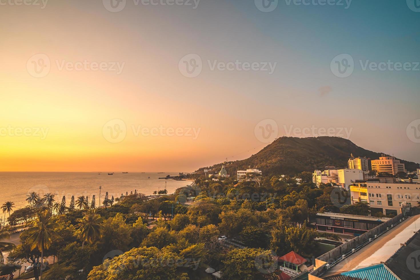 Vung Tau city aerial view with beautiful sunset and so many boats. Panoramic coastal Vung Tau view from above, with waves, coastline, streets, coconut trees and Tao Phung mountain in Vietnam. photo