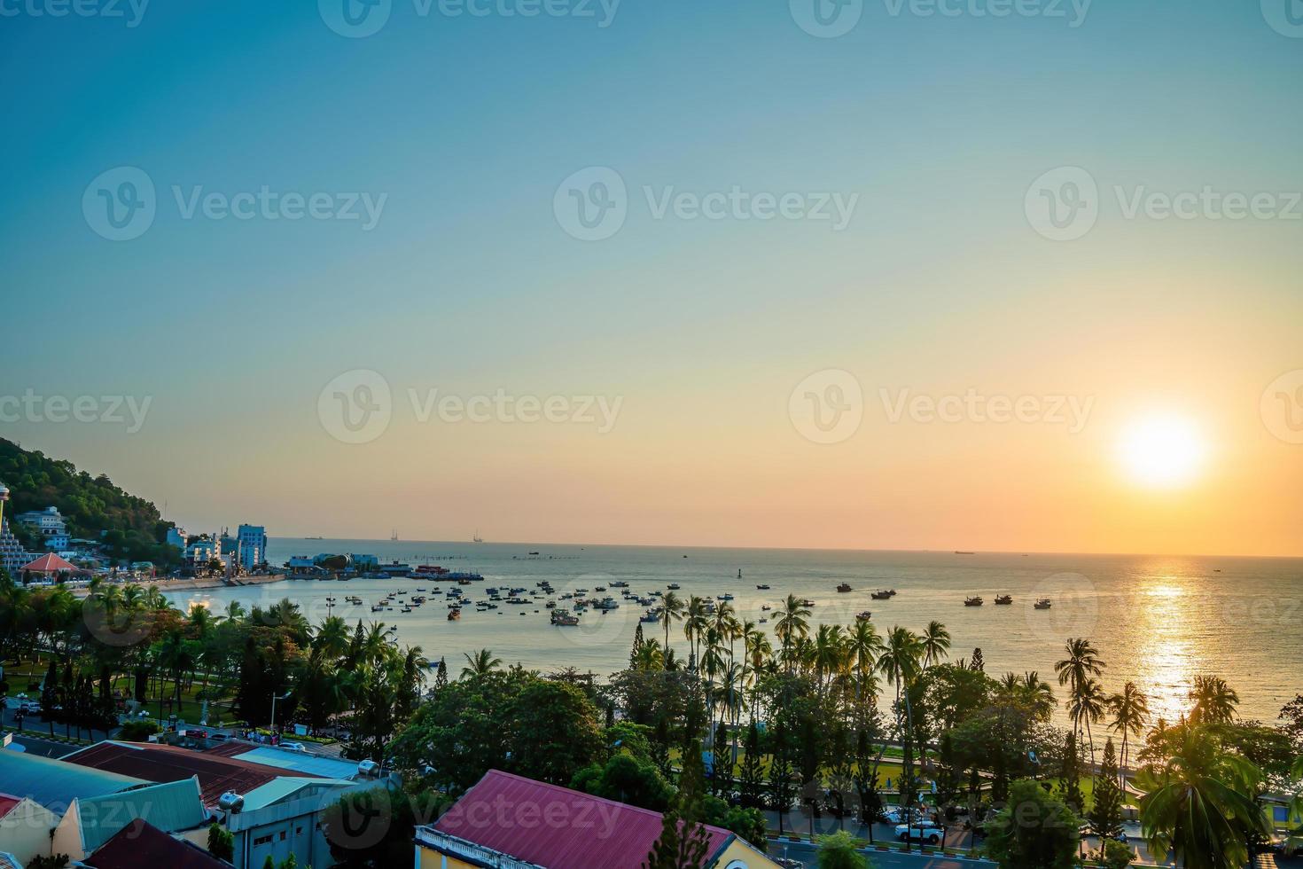 Vung Tau city aerial view with beautiful sunset and so many boats. Panoramic coastal Vung Tau view from above, with waves, coastline, streets, coconut trees and Tao Phung mountain in Vietnam. photo