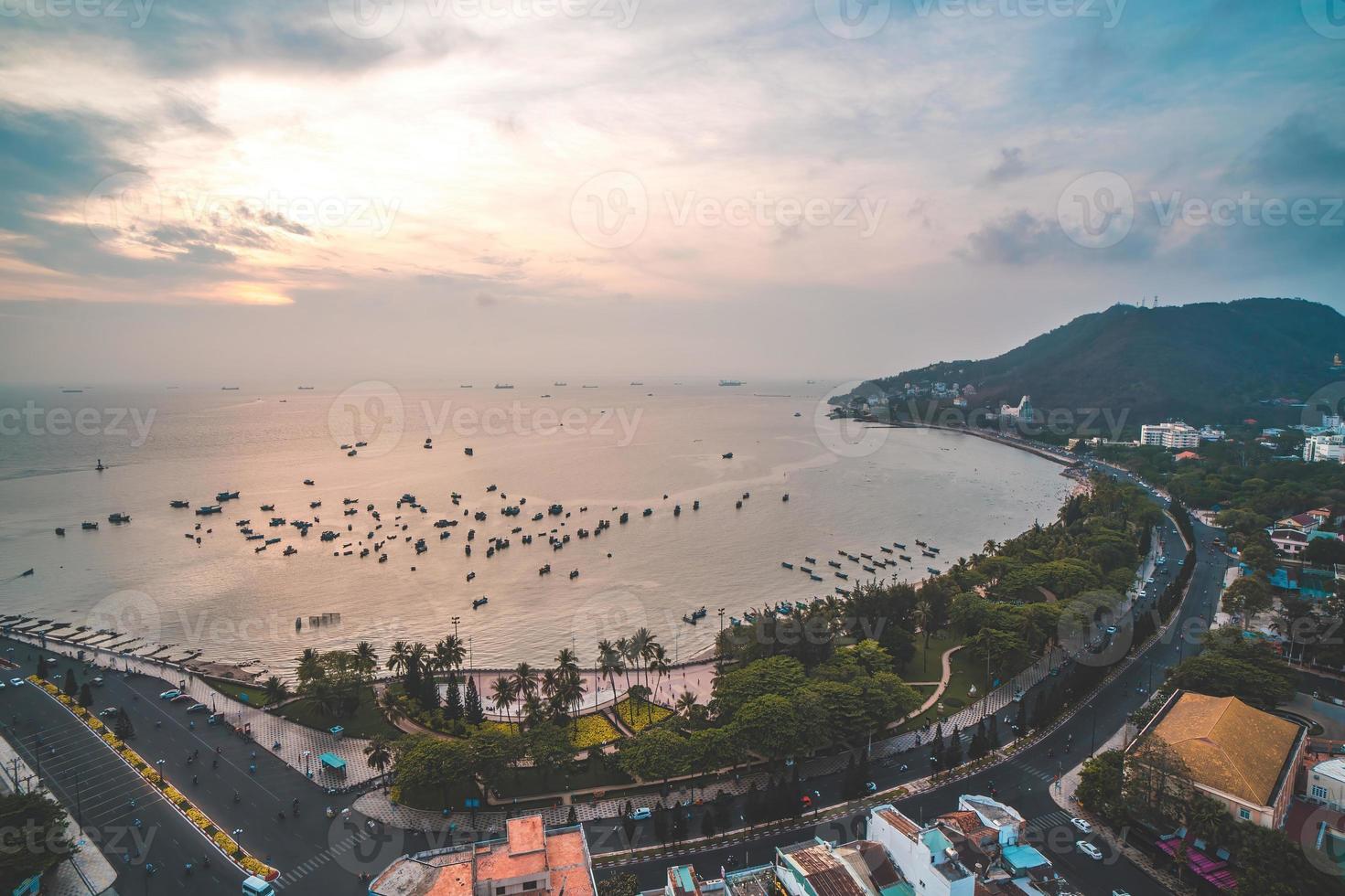 Vung Tau city aerial view with beautiful sunset and so many boats. Panoramic coastal Vung Tau view from above, with waves, coastline, streets, coconut trees and Tao Phung mountain in Vietnam. photo