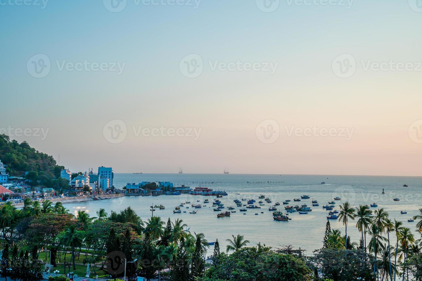 Vung Tau city aerial view with beautiful sunset and so many boats. Panoramic coastal Vung Tau view from above, with waves, coastline, streets, coconut trees and Tao Phung mountain in Vietnam. photo