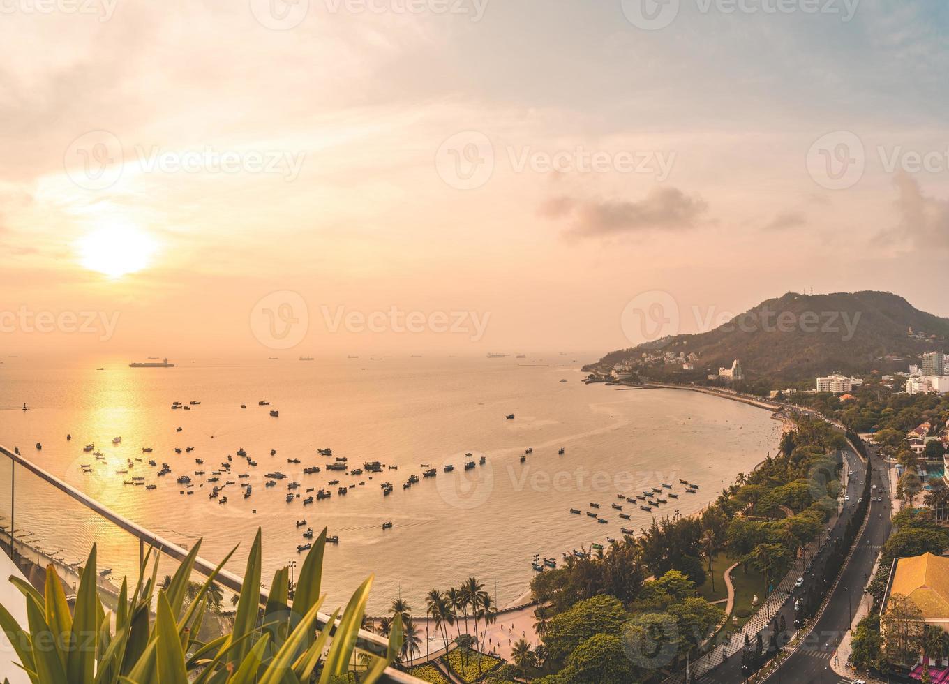 Vung Tau city aerial view with beautiful sunset and so many boats. Panoramic coastal Vung Tau view from above, with waves, coastline, streets, coconut trees and Tao Phung mountain in Vietnam. photo