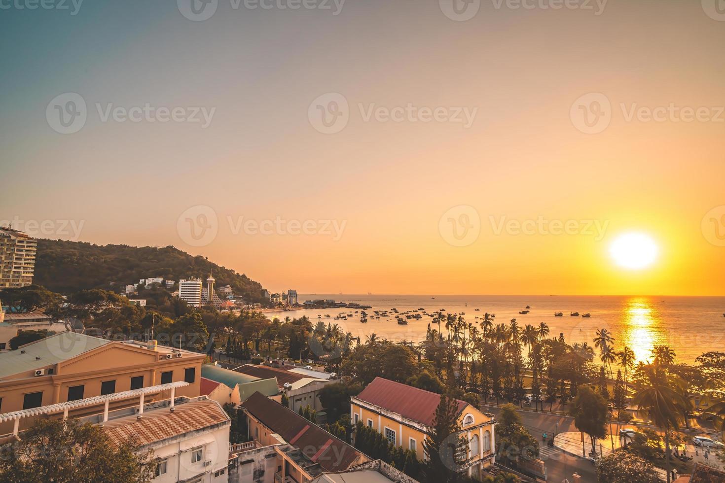 Vung Tau city aerial view with beautiful sunset and so many boats. Panoramic coastal Vung Tau view from above, with waves, coastline, streets, coconut trees and Tao Phung mountain in Vietnam. photo