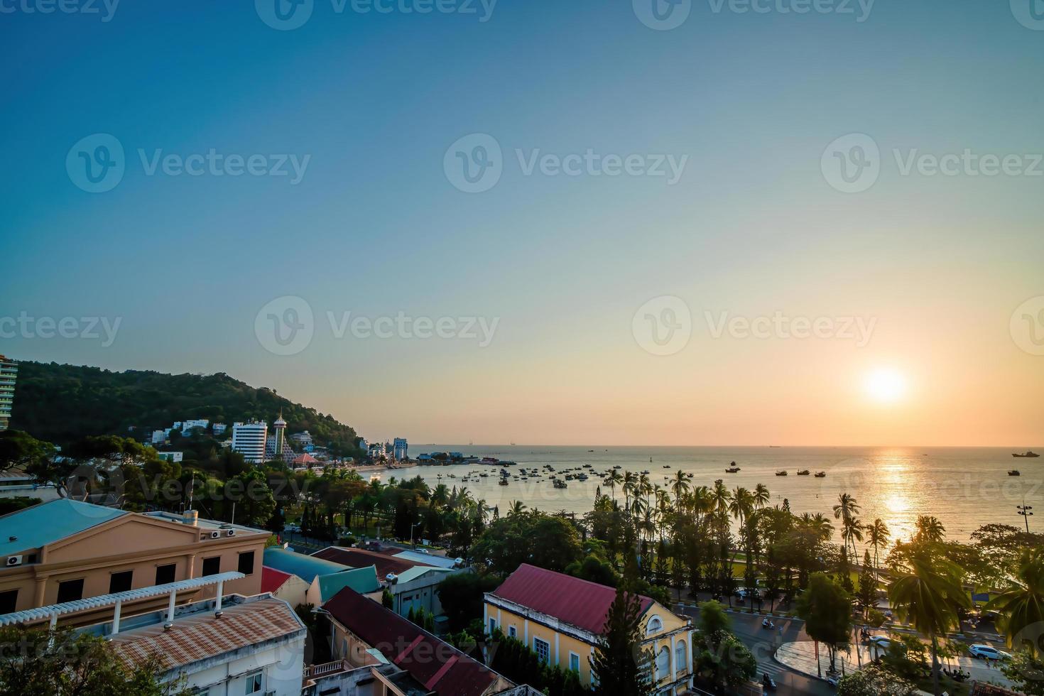 Vung Tau city aerial view with beautiful sunset and so many boats. Panoramic coastal Vung Tau view from above, with waves, coastline, streets, coconut trees and Tao Phung mountain in Vietnam. photo