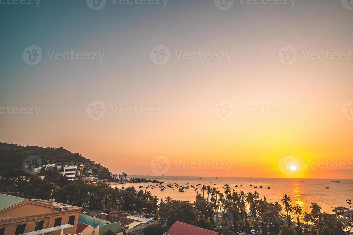 Vung Tau city aerial view with beautiful sunset and so many boats. Panoramic coastal Vung Tau view from above, with waves, coastline, streets, coconut trees and Tao Phung mountain in Vietnam. photo