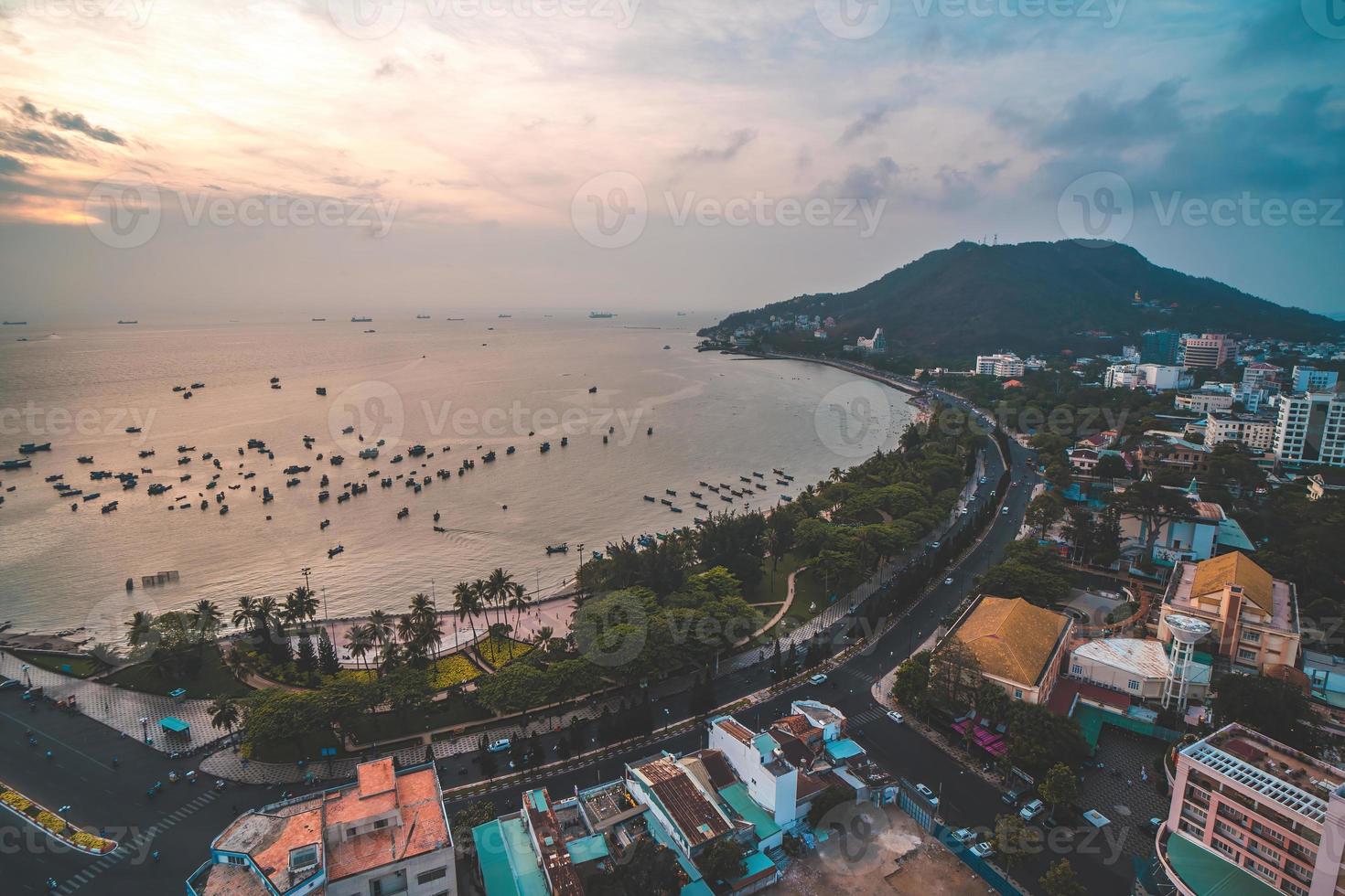 Vung Tau city aerial view with beautiful sunset and so many boats. Panoramic coastal Vung Tau view from above, with waves, coastline, streets, coconut trees and Tao Phung mountain in Vietnam. photo
