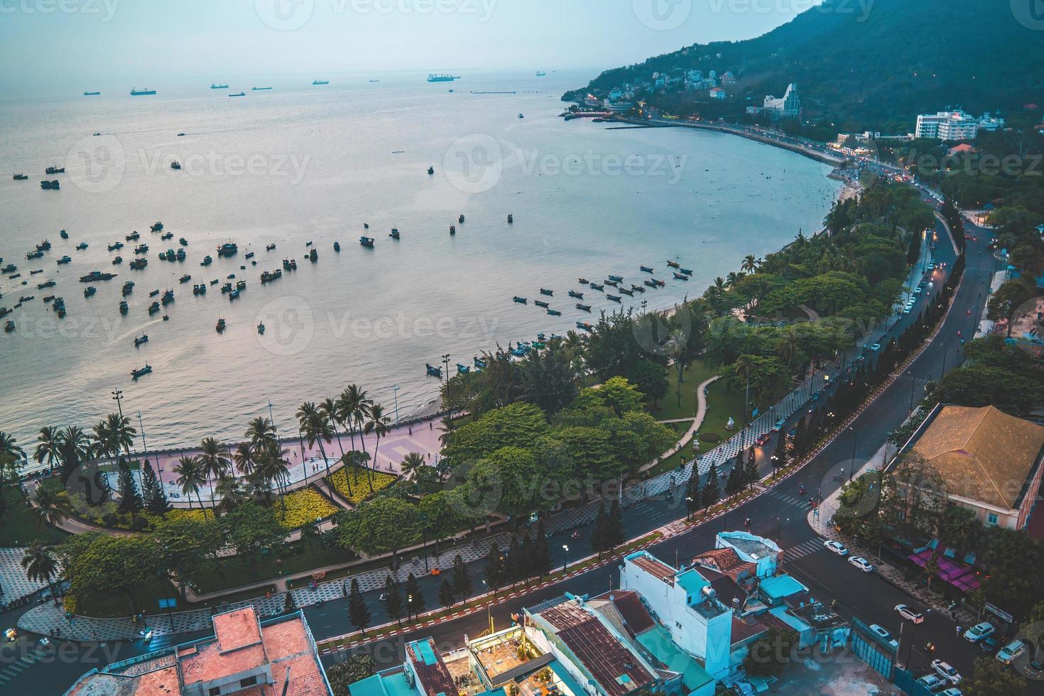 Vung Tau city aerial view with beautiful sunset and so many boats. Panoramic coastal Vung Tau view from above, with waves, coastline, streets, coconut trees and Tao Phung mountain in Vietnam. photo