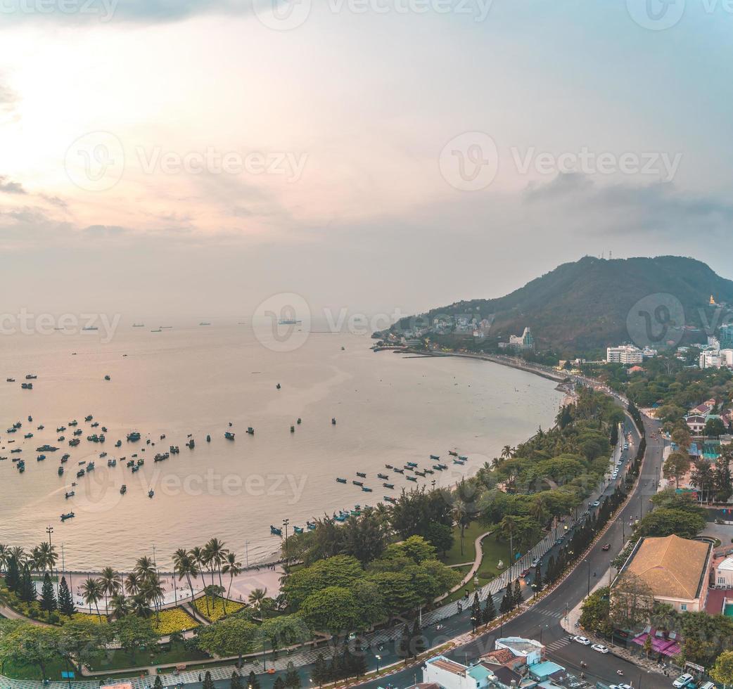 Vung Tau city aerial view with beautiful sunset and so many boats. Panoramic coastal Vung Tau view from above, with waves, coastline, streets, coconut trees and Tao Phung mountain in Vietnam. photo