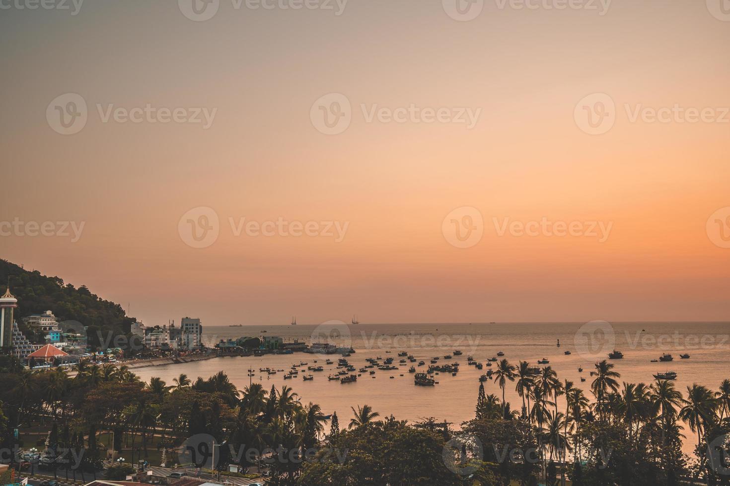Vung Tau city aerial view with beautiful sunset and so many boats. Panoramic coastal Vung Tau view from above, with waves, coastline, streets, coconut trees and Tao Phung mountain in Vietnam. photo