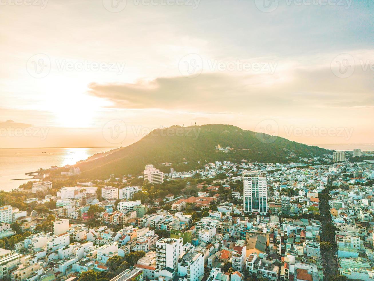 Vung Tau city aerial view with beautiful sunset and so many boats. Panoramic coastal Vung Tau view from above, with waves, coastline, streets, coconut trees and Tao Phung mountain in Vietnam. photo