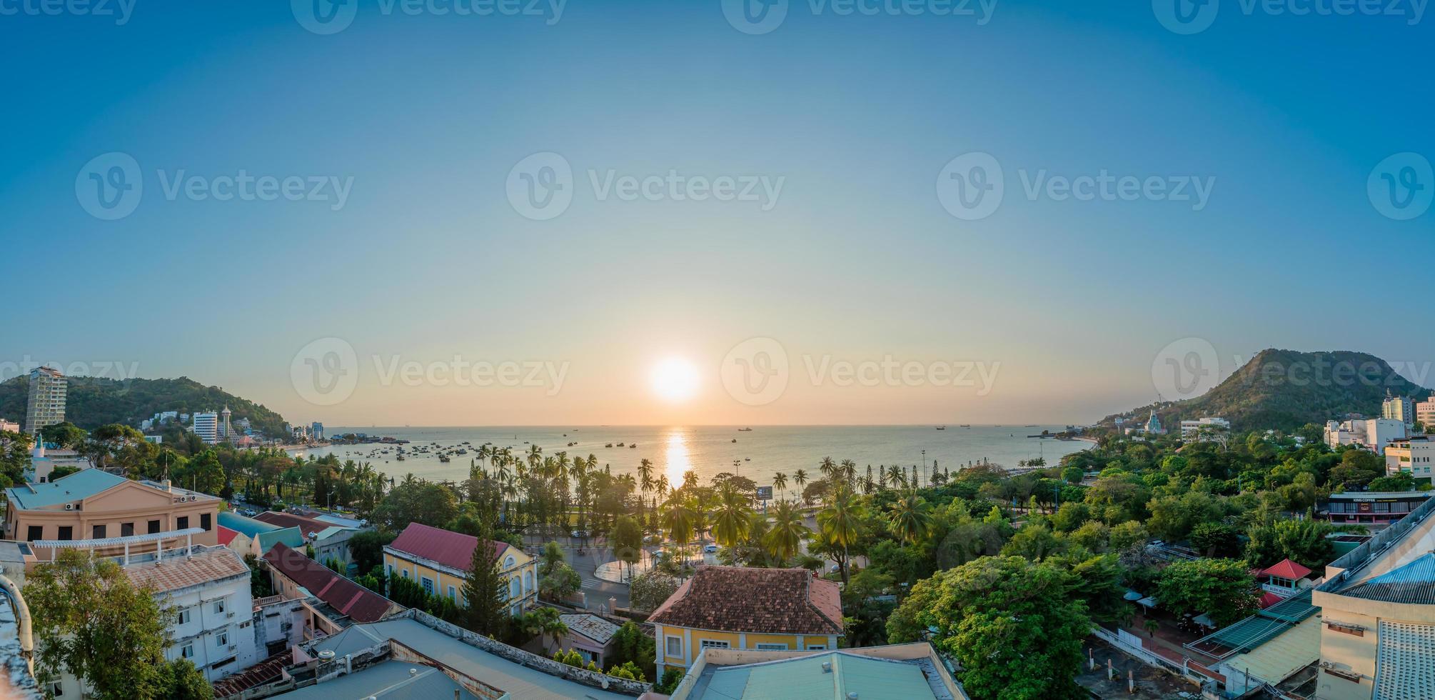 Vung Tau city aerial view with beautiful sunset and so many boats. Panoramic coastal Vung Tau view from above, with waves, coastline, streets, coconut trees and Tao Phung mountain in Vietnam. photo