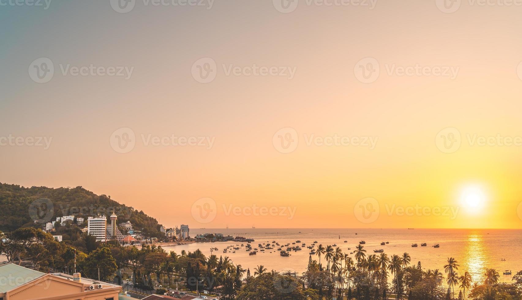 Vung Tau city aerial view with beautiful sunset and so many boats. Panoramic coastal Vung Tau view from above, with waves, coastline, streets, coconut trees and Tao Phung mountain in Vietnam. photo