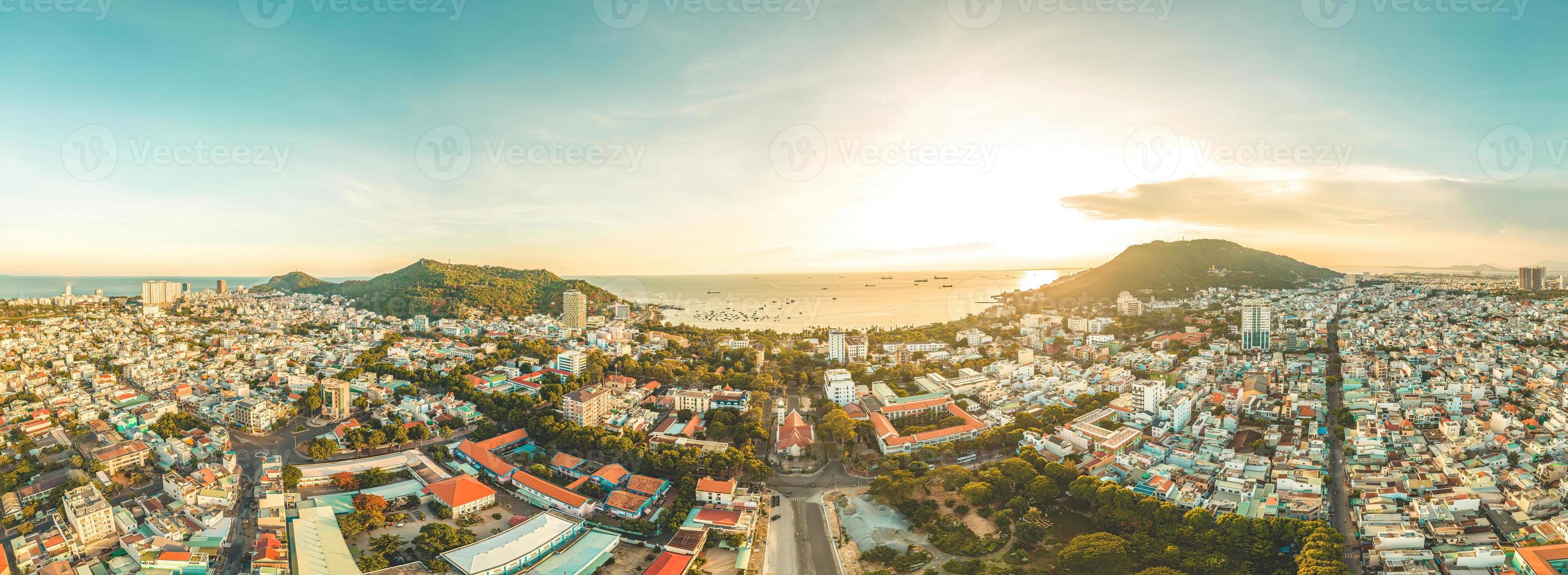 vista aérea de la ciudad de vung tau con hermosa puesta de sol y tantos barcos. vista panorámica costera de vung tau desde arriba, con olas, costa, calles, cocoteros y montaña tao phung en vietnam. foto