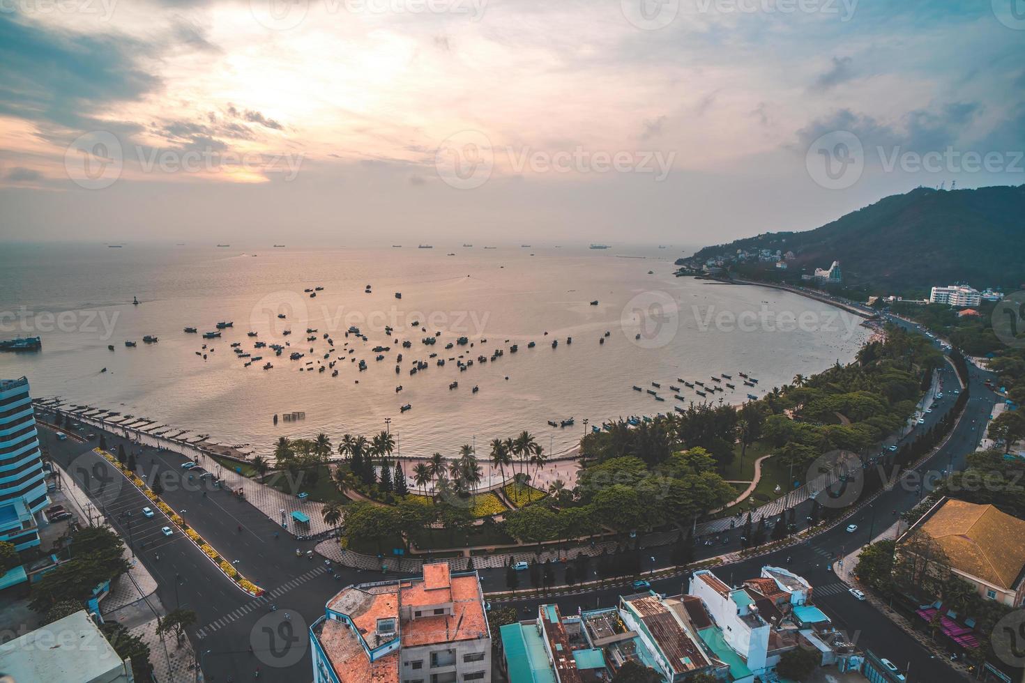 Vung Tau city aerial view with beautiful sunset and so many boats. Panoramic coastal Vung Tau view from above, with waves, coastline, streets, coconut trees and Tao Phung mountain in Vietnam. photo