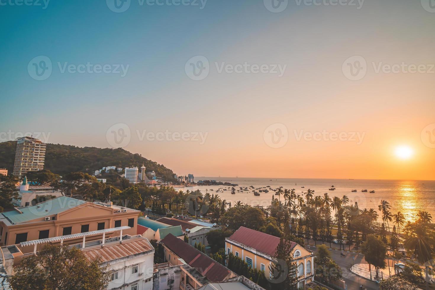 Vung Tau city aerial view with beautiful sunset and so many boats. Panoramic coastal Vung Tau view from above, with waves, coastline, streets, coconut trees and Tao Phung mountain in Vietnam. photo