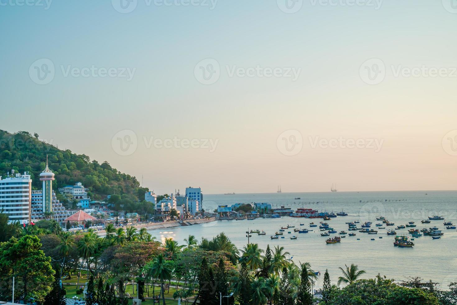 Vung Tau city aerial view with beautiful sunset and so many boats. Panoramic coastal Vung Tau view from above, with waves, coastline, streets, coconut trees and Tao Phung mountain in Vietnam. photo