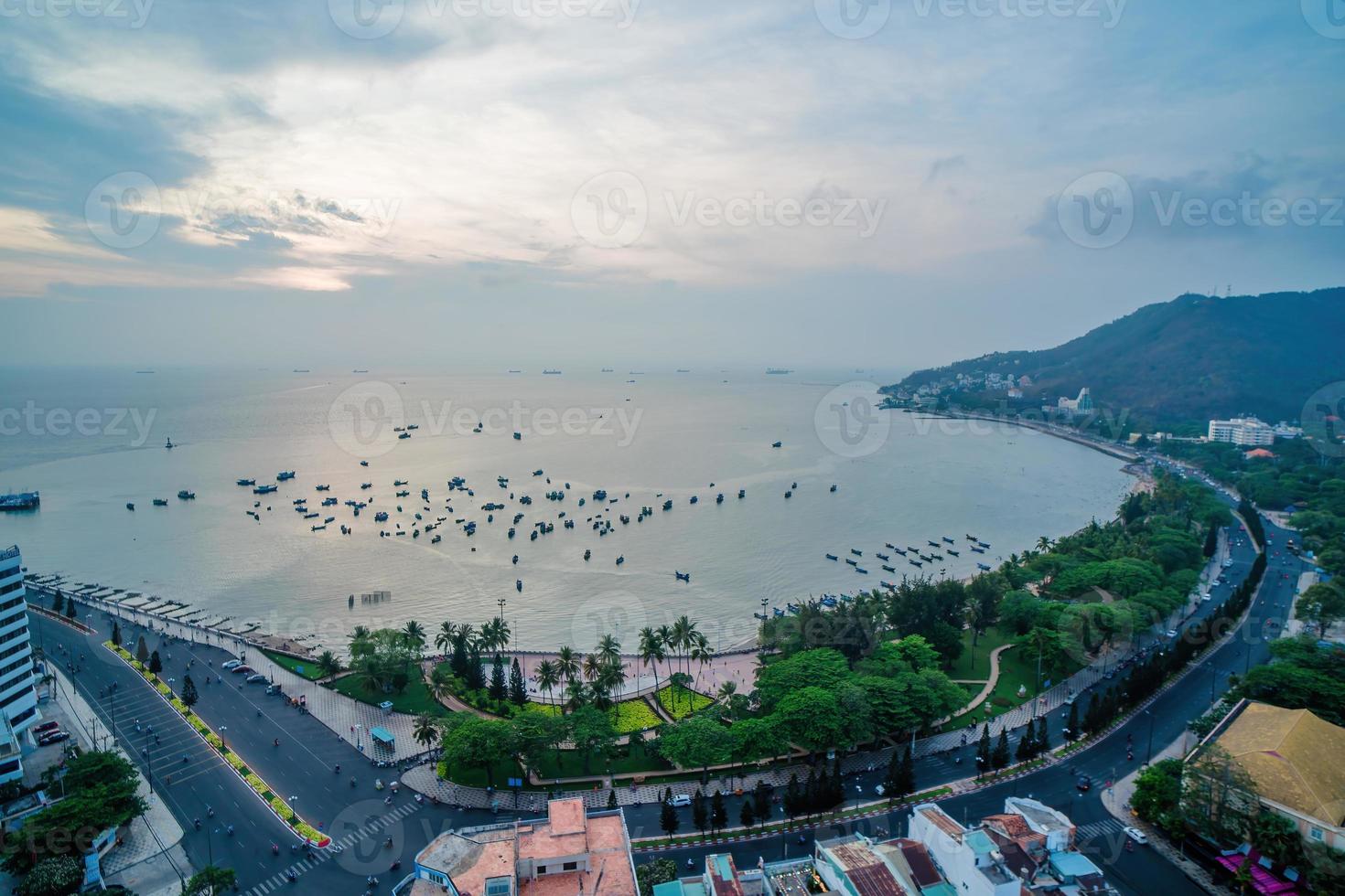 Vung Tau city aerial view with beautiful sunset and so many boats. Panoramic coastal Vung Tau view from above, with waves, coastline, streets, coconut trees and Tao Phung mountain in Vietnam. photo