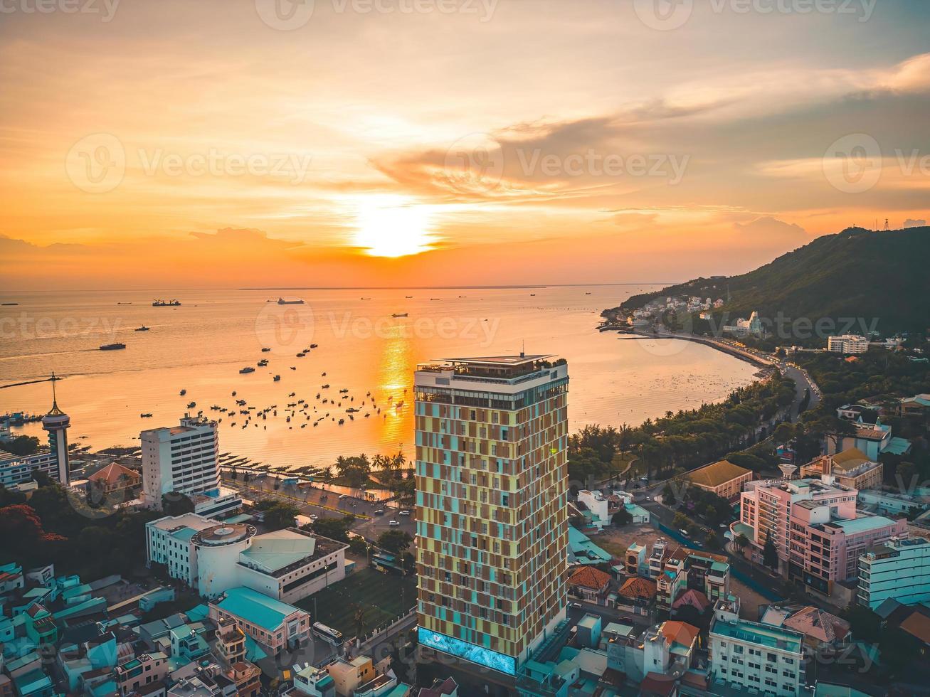 Vung Tau city aerial view with beautiful sunset and so many boats. Panoramic coastal Vung Tau view from above, with waves, coastline, streets, coconut trees and Tao Phung mountain in Vietnam. photo
