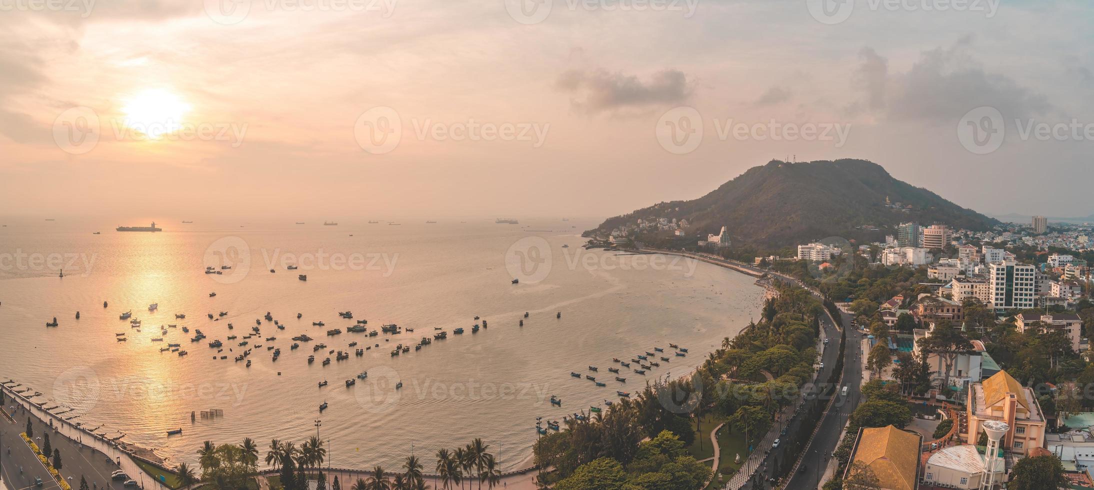 Vung Tau city aerial view with beautiful sunset and so many boats. Panoramic coastal Vung Tau view from above, with waves, coastline, streets, coconut trees and Tao Phung mountain in Vietnam. photo