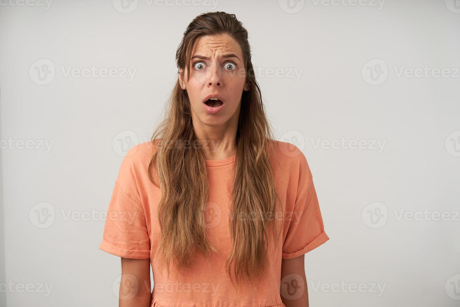 Portrait of scared young female posing over white background with wide eyes and mouth opened, wearing casual hairstyle and natural make-up photo