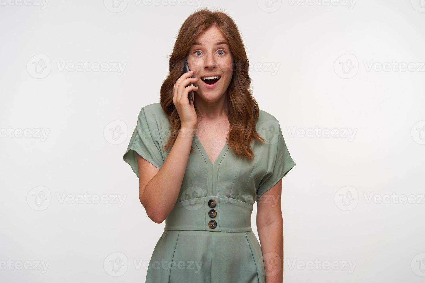 Surprised pretty woman with romantic hairstyle looking to camera with wide mouth opened, raising eyebrows because of hearing amazing positive news, isolated over white background photo