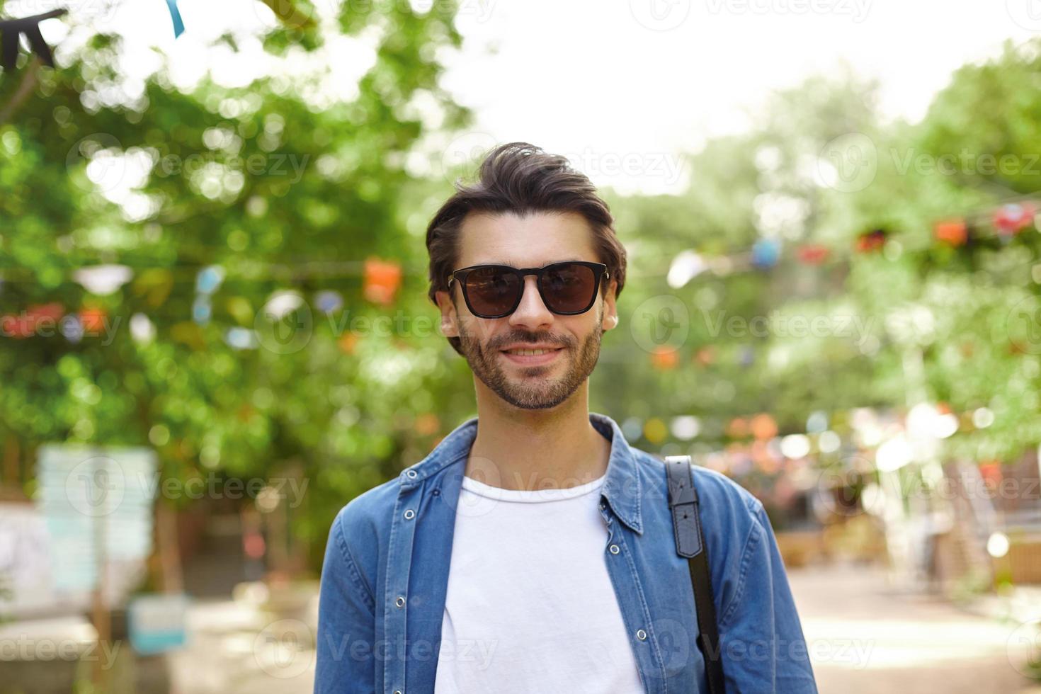 Good looking young dark haired male with beard wearing casual clothes and sunglasses photo