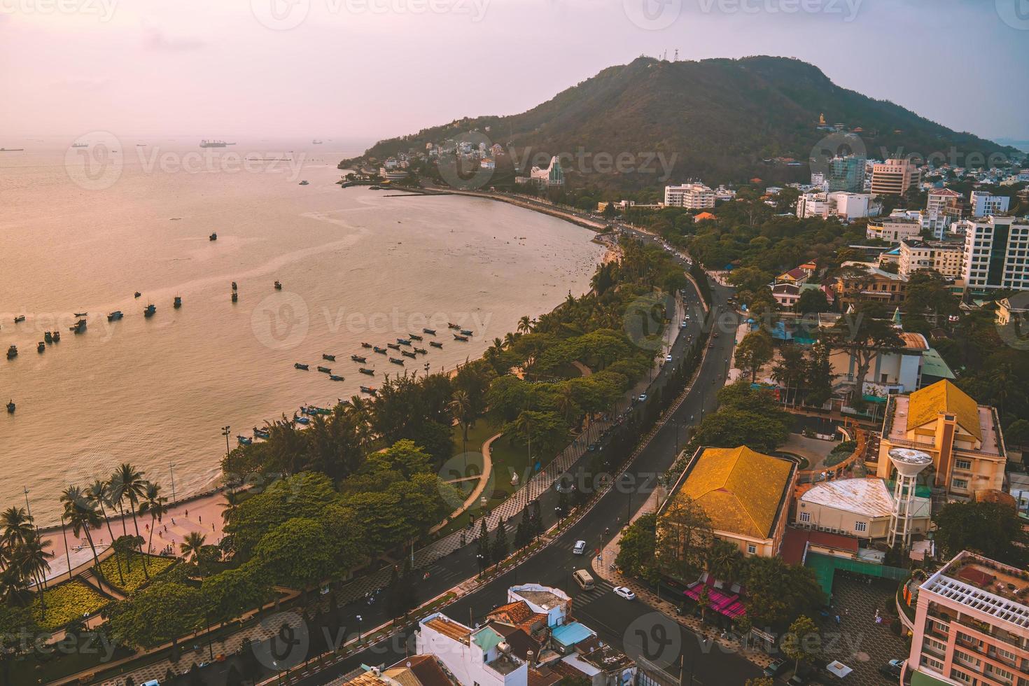 Vung Tau city aerial view with beautiful sunset and so many boats. Panoramic coastal Vung Tau view from above, with waves, coastline, streets, coconut trees and Tao Phung mountain in Vietnam. photo
