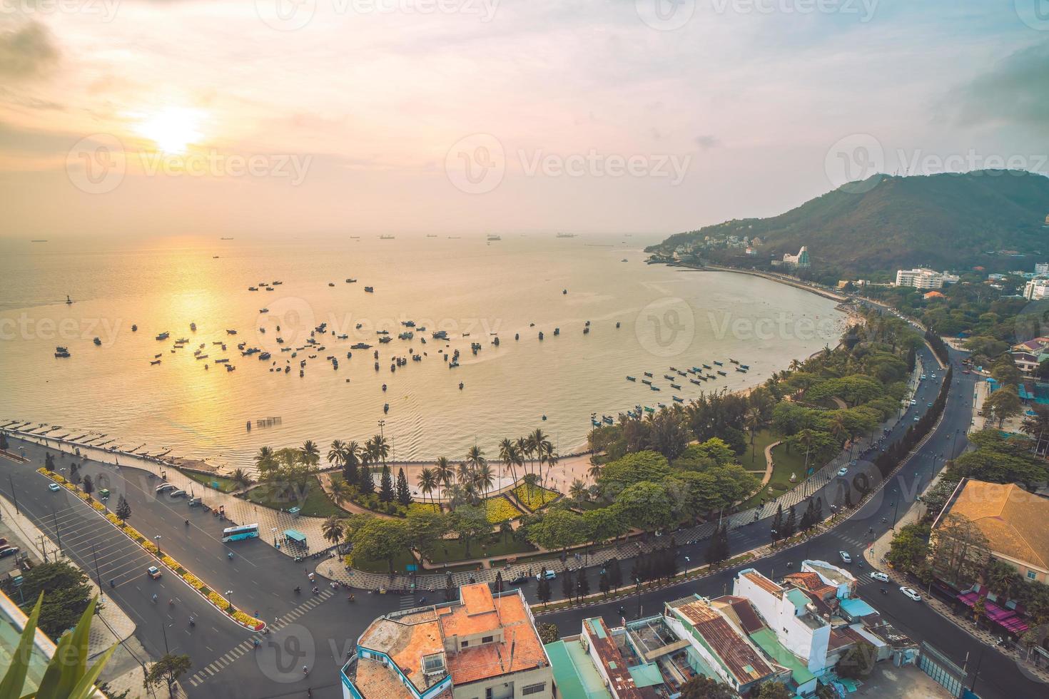 Vung Tau city aerial view with beautiful sunset and so many boats. Panoramic coastal Vung Tau view from above, with waves, coastline, streets, coconut trees and Tao Phung mountain in Vietnam. photo