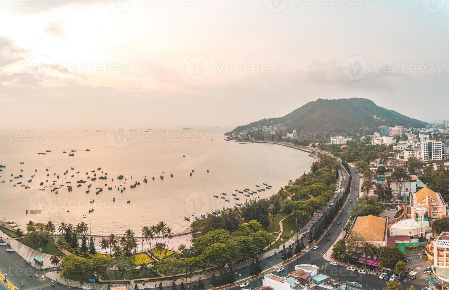 Vung Tau city aerial view with beautiful sunset and so many boats. Panoramic coastal Vung Tau view from above, with waves, coastline, streets, coconut trees and Tao Phung mountain in Vietnam. photo