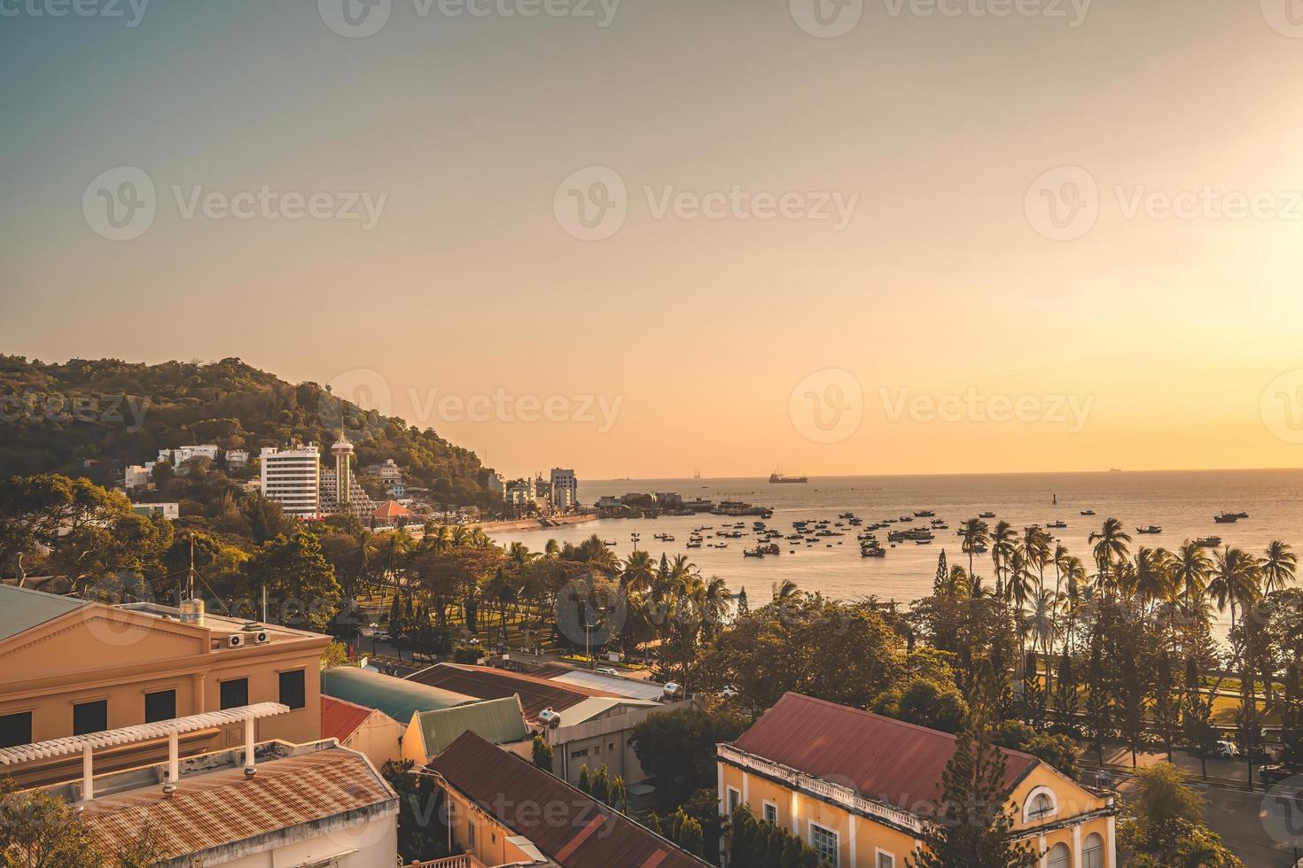 Vung Tau city aerial view with beautiful sunset and so many boats. Panoramic coastal Vung Tau view from above, with waves, coastline, streets, coconut trees and Tao Phung mountain in Vietnam. photo