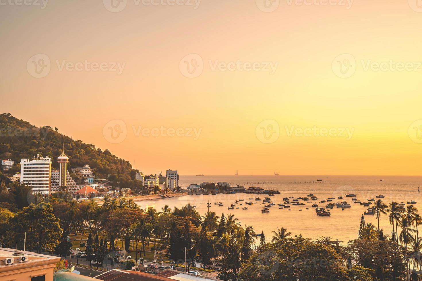 vista aérea de la ciudad de vung tau con hermosa puesta de sol y tantos barcos. vista panorámica costera de vung tau desde arriba, con olas, costa, calles, cocoteros y montaña tao phung en vietnam. foto