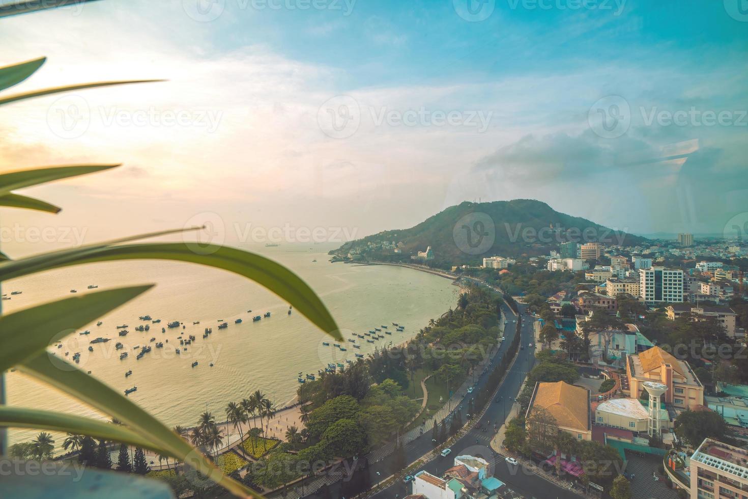 Vung Tau city aerial view with beautiful sunset and so many boats. Panoramic coastal Vung Tau view from above, with waves, coastline, streets, coconut trees and Tao Phung mountain in Vietnam. photo