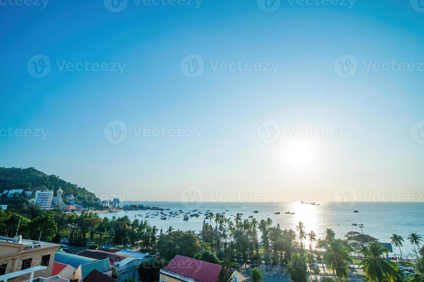Vung Tau city aerial view with beautiful sunset and so many boats. Panoramic coastal Vung Tau view from above, with waves, coastline, streets, coconut trees and Tao Phung mountain in Vietnam. photo