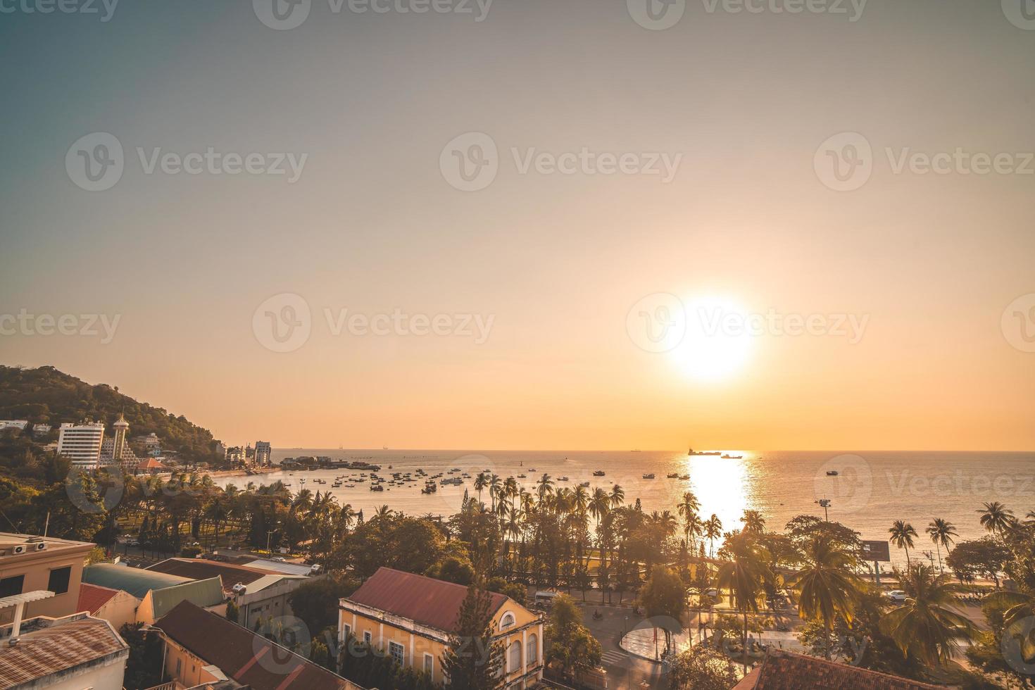 Vung Tau city aerial view with beautiful sunset and so many boats. Panoramic coastal Vung Tau view from above, with waves, coastline, streets, coconut trees and Tao Phung mountain in Vietnam. photo