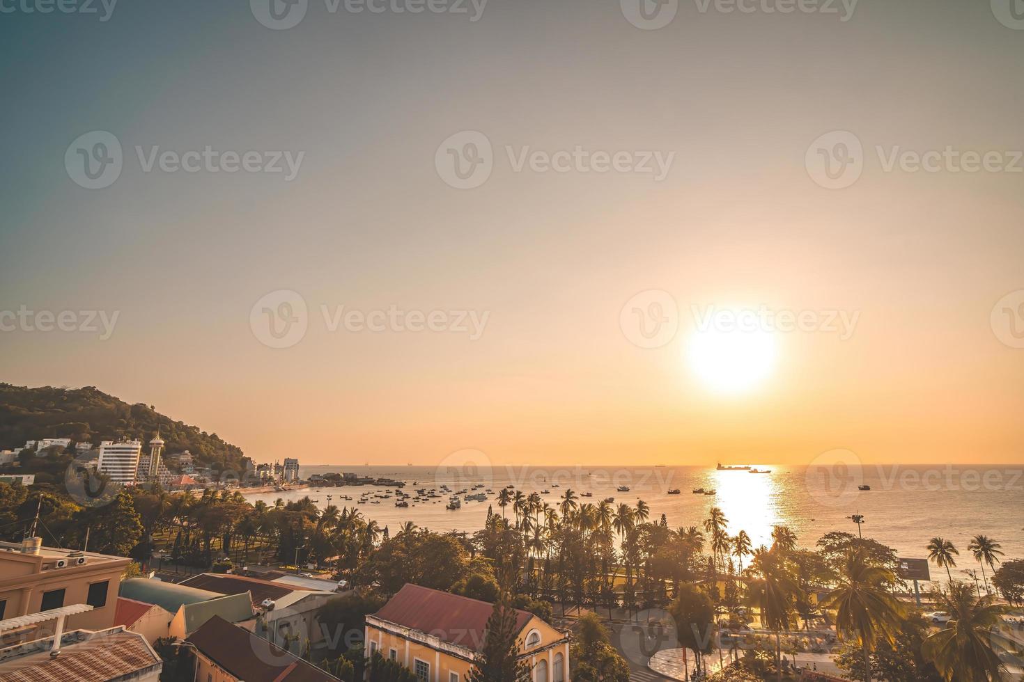 Vung Tau city aerial view with beautiful sunset and so many boats. Panoramic coastal Vung Tau view from above, with waves, coastline, streets, coconut trees and Tao Phung mountain in Vietnam. photo