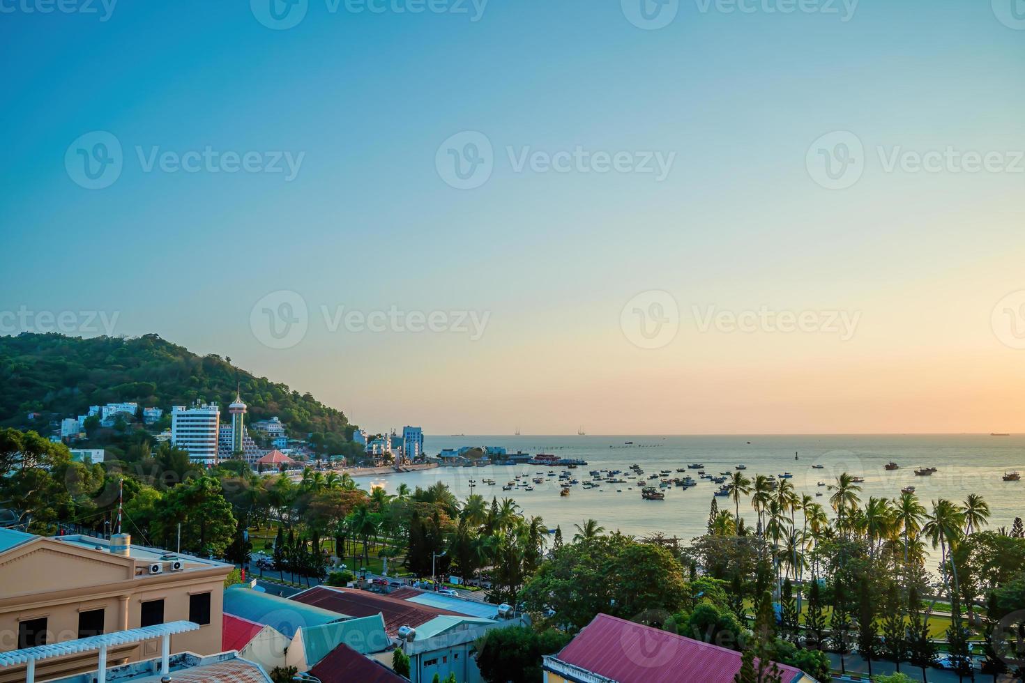 Vung Tau city aerial view with beautiful sunset and so many boats. Panoramic coastal Vung Tau view from above, with waves, coastline, streets, coconut trees and Tao Phung mountain in Vietnam. photo