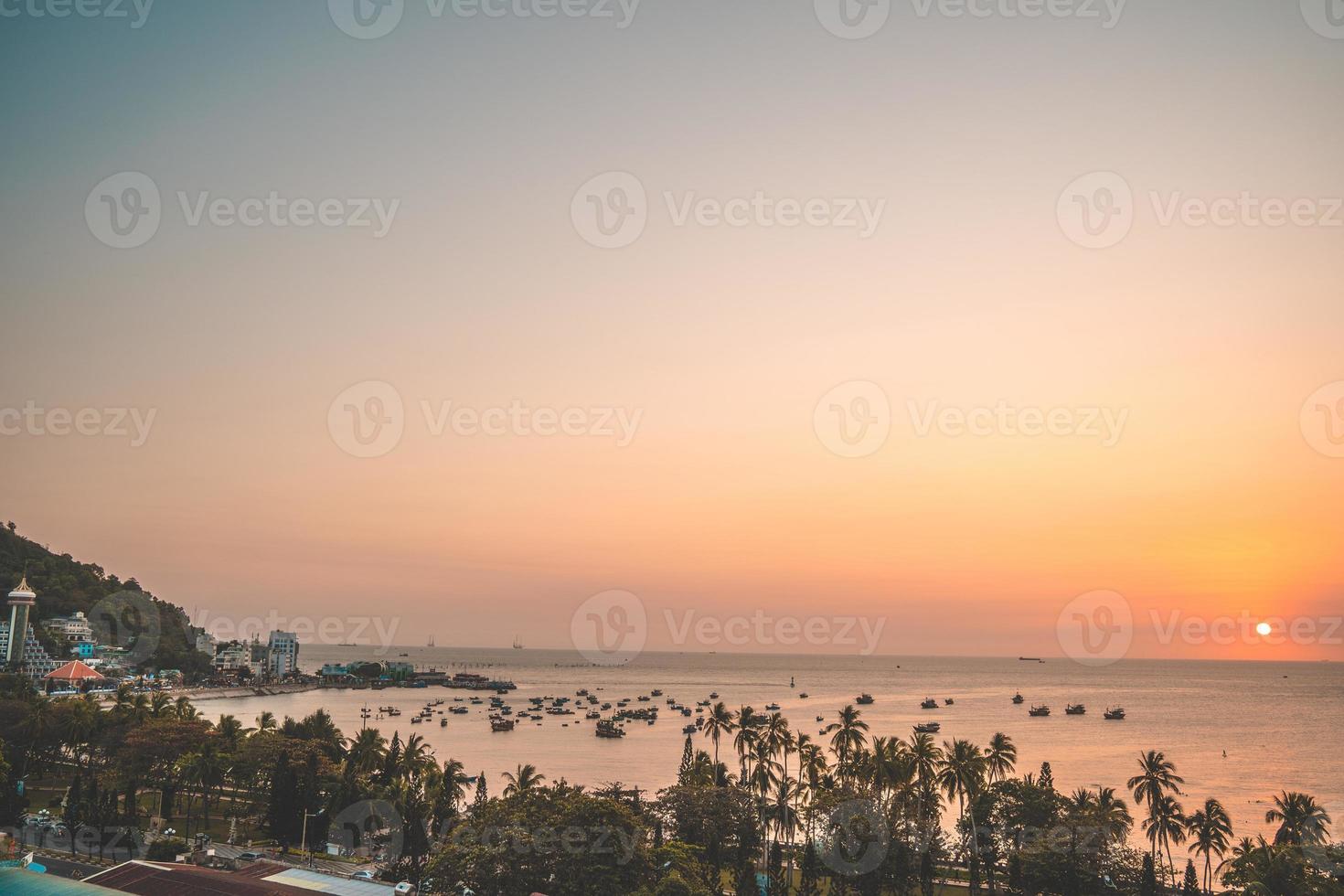 Vung Tau city aerial view with beautiful sunset and so many boats. Panoramic coastal Vung Tau view from above, with waves, coastline, streets, coconut trees and Tao Phung mountain in Vietnam. photo