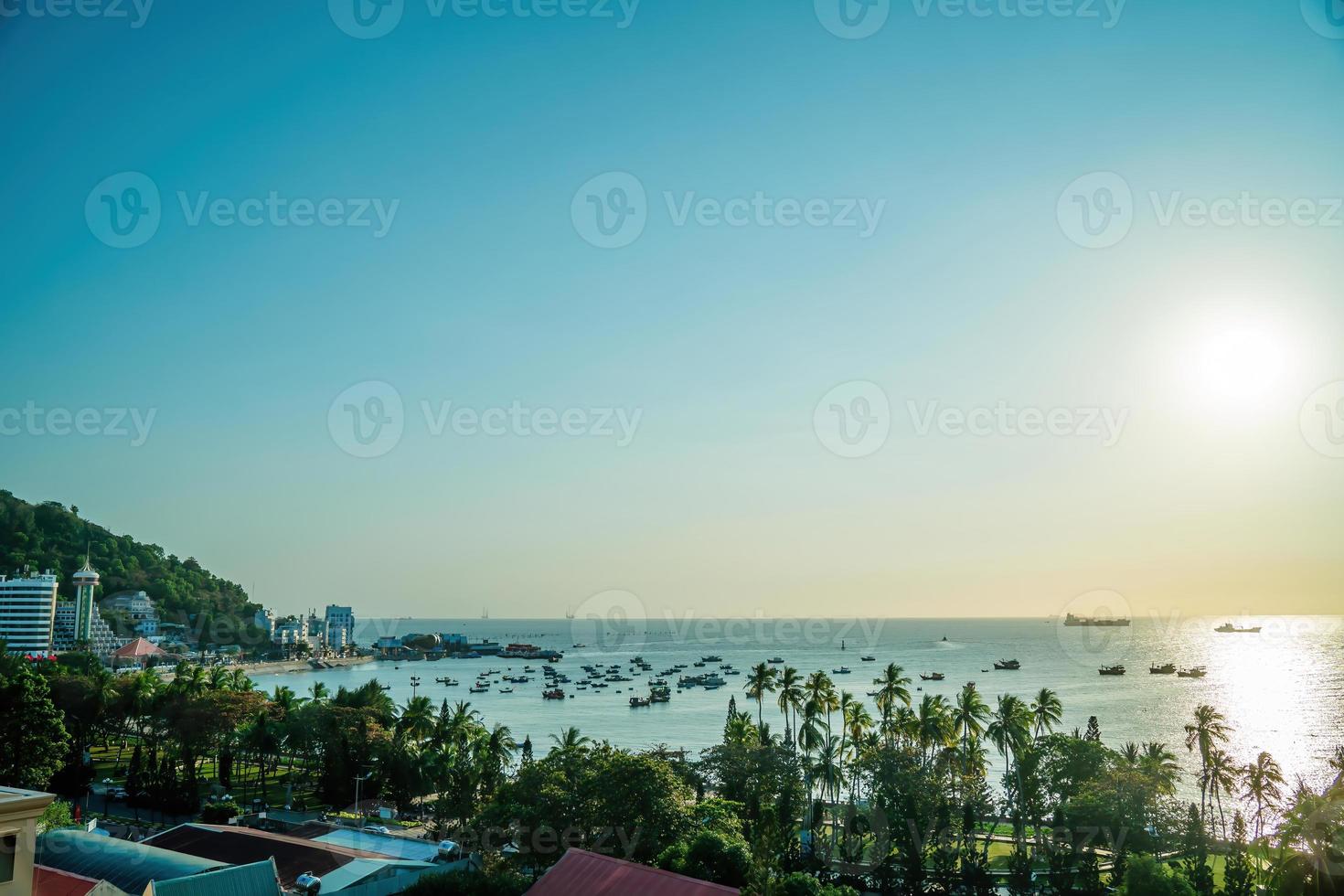 vista aérea de la ciudad de vung tau con hermosa puesta de sol y tantos barcos. vista panorámica costera de vung tau desde arriba, con olas, costa, calles, cocoteros y montaña tao phung en vietnam. foto