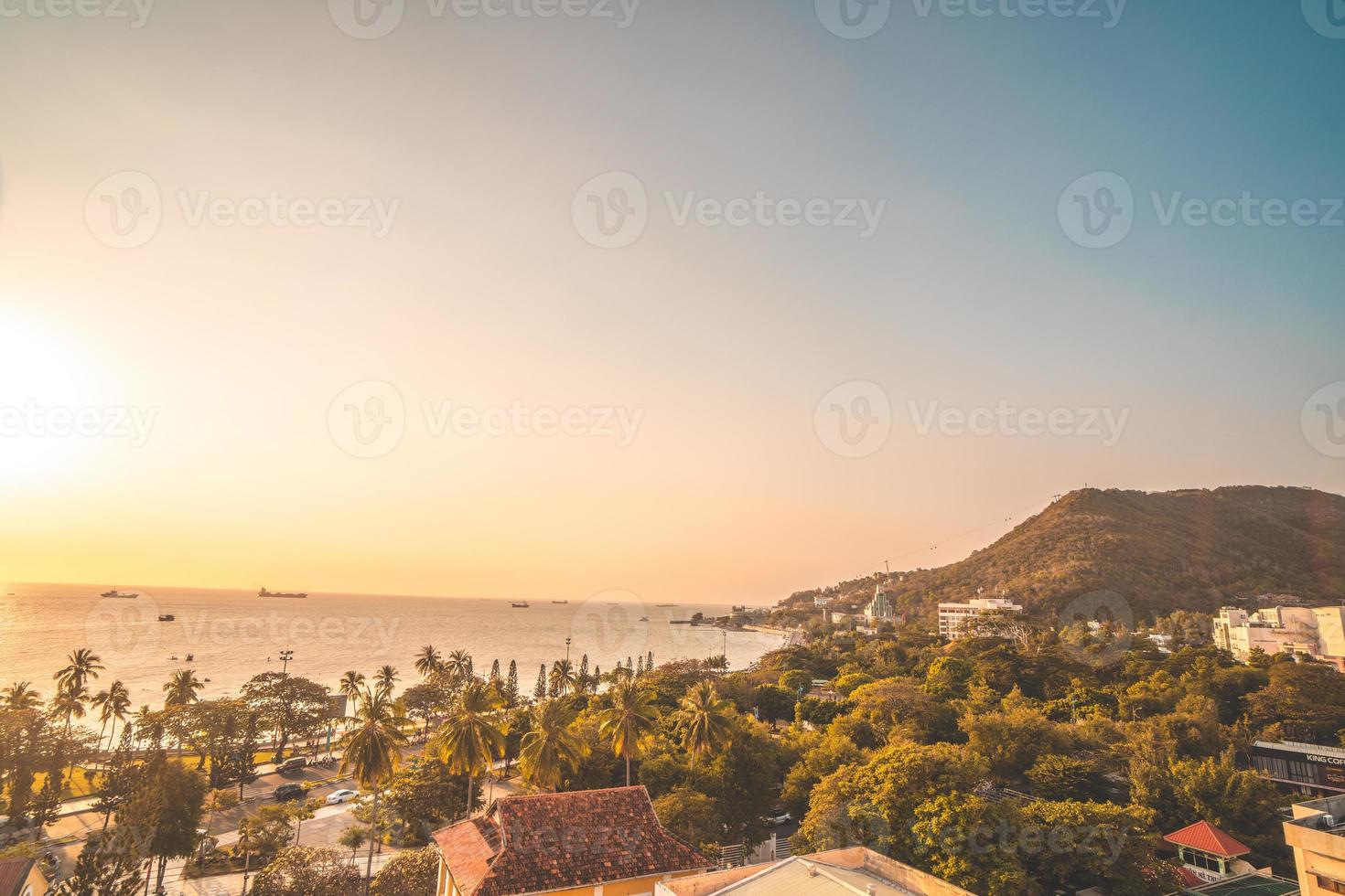 vista aérea de la ciudad de vung tau con hermosa puesta de sol y tantos barcos. vista panorámica costera de vung tau desde arriba, con olas, costa, calles, cocoteros y montaña tao phung en vietnam. foto