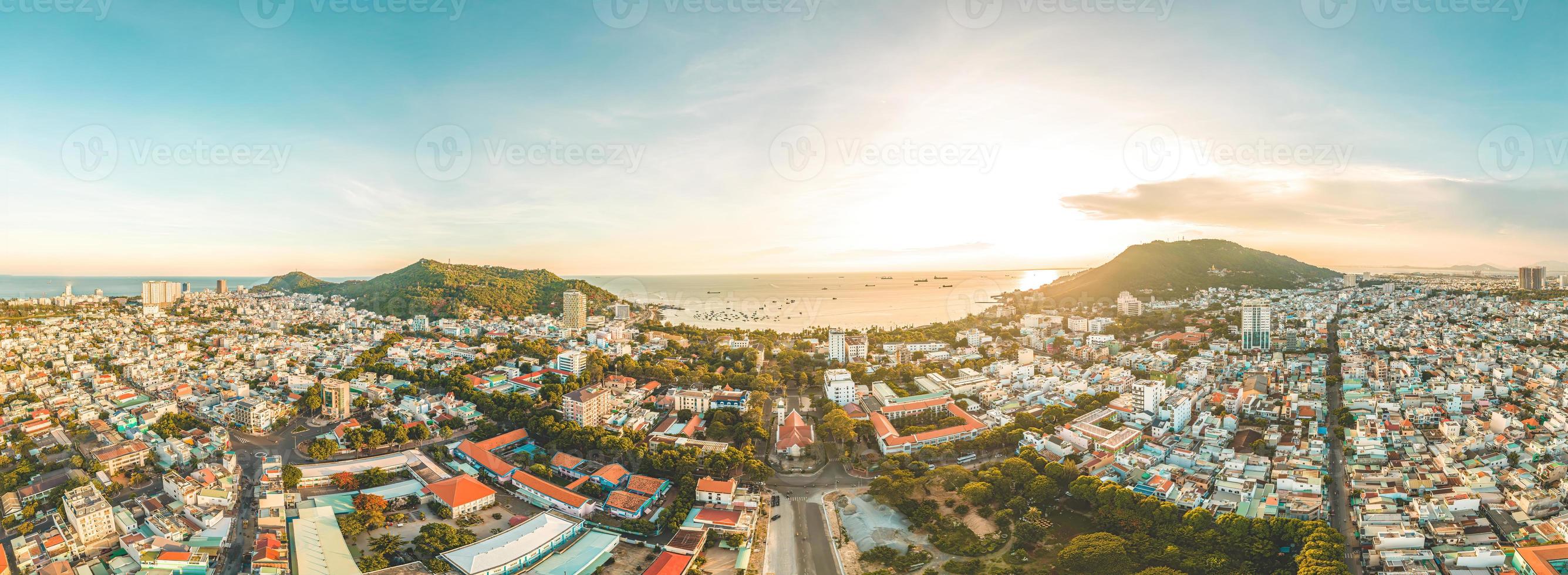 Vung Tau city aerial view with beautiful sunset and so many boats. Panoramic coastal Vung Tau view from above, with waves, coastline, streets, coconut trees and Tao Phung mountain in Vietnam. photo