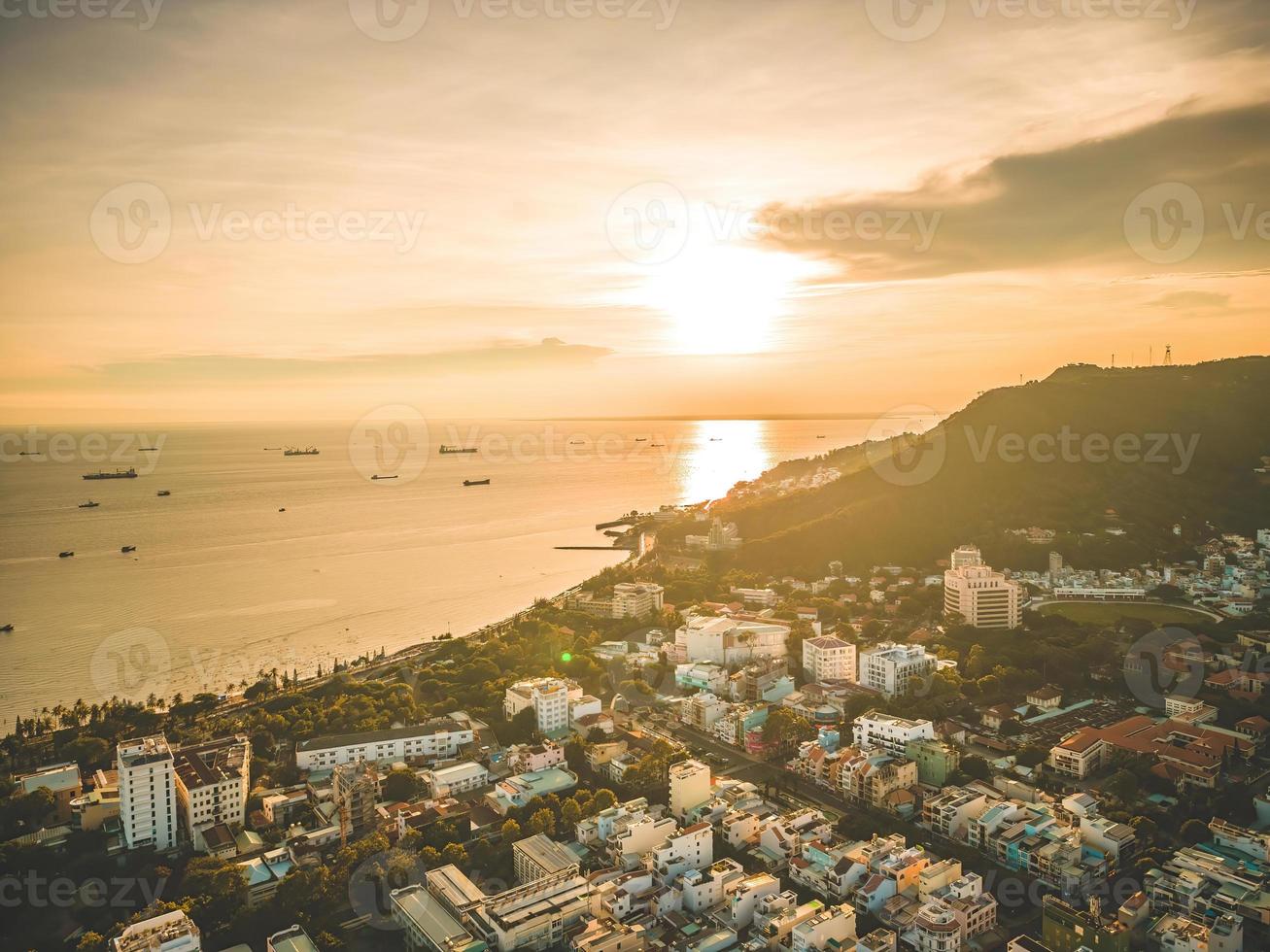 vista aérea de la ciudad de vung tau con hermosa puesta de sol y tantos barcos. vista panorámica costera de vung tau desde arriba, con olas, costa, calles, cocoteros y montaña tao phung en vietnam. foto