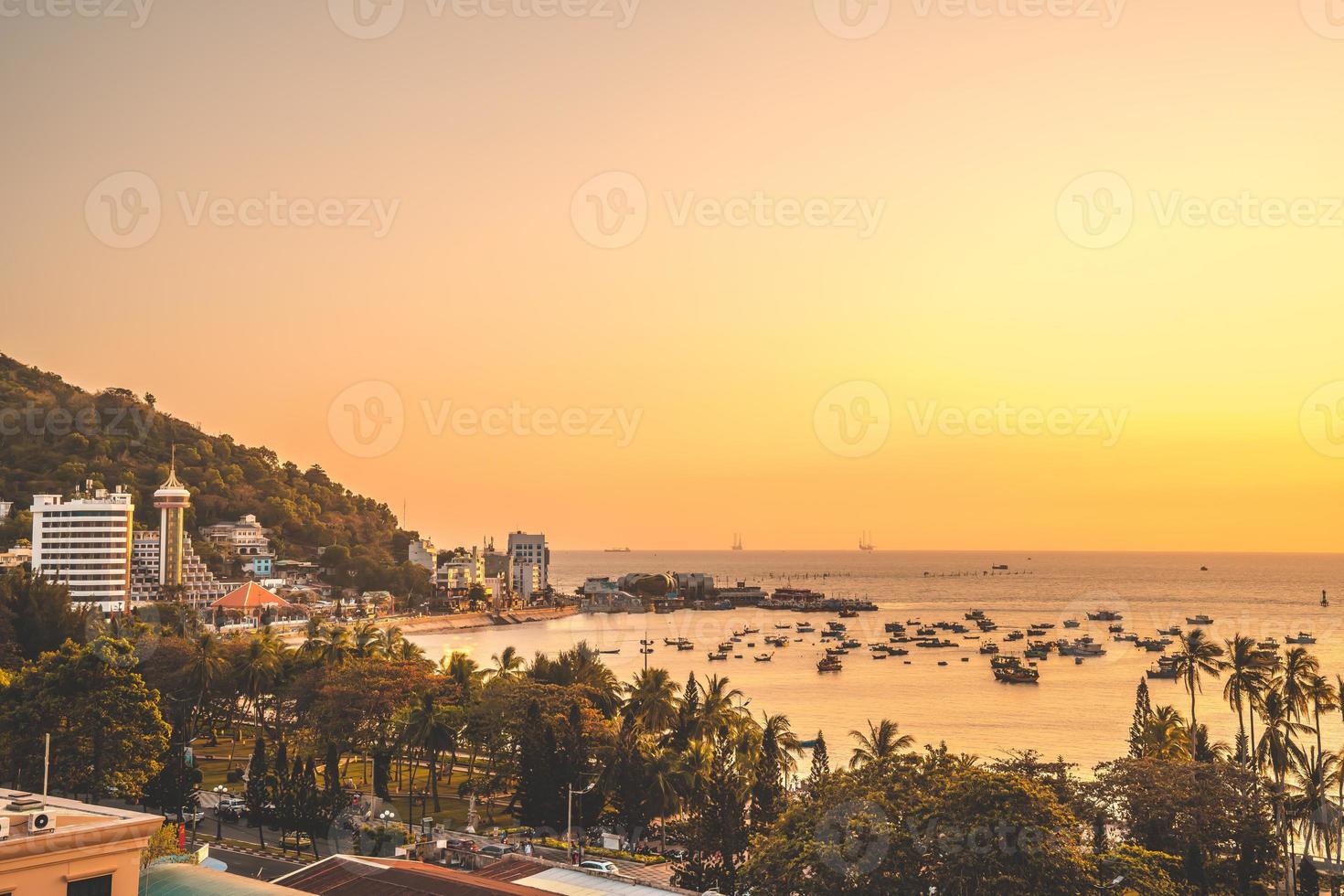 vista aérea de la ciudad de vung tau con hermosa puesta de sol y tantos barcos. vista panorámica costera de vung tau desde arriba, con olas, costa, calles, cocoteros y montaña tao phung en vietnam. foto