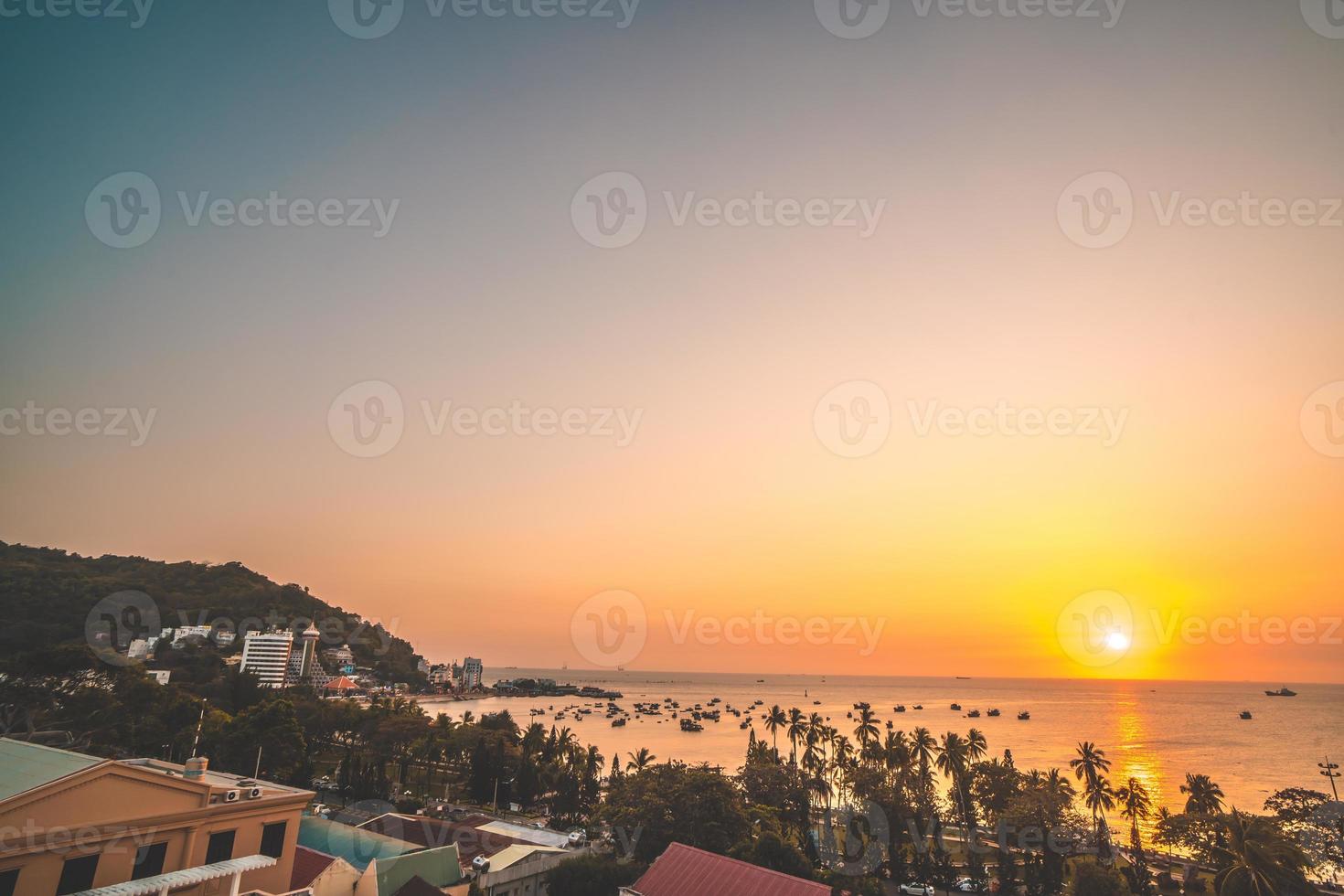 Vung Tau city aerial view with beautiful sunset and so many boats. Panoramic coastal Vung Tau view from above, with waves, coastline, streets, coconut trees and Tao Phung mountain in Vietnam. photo