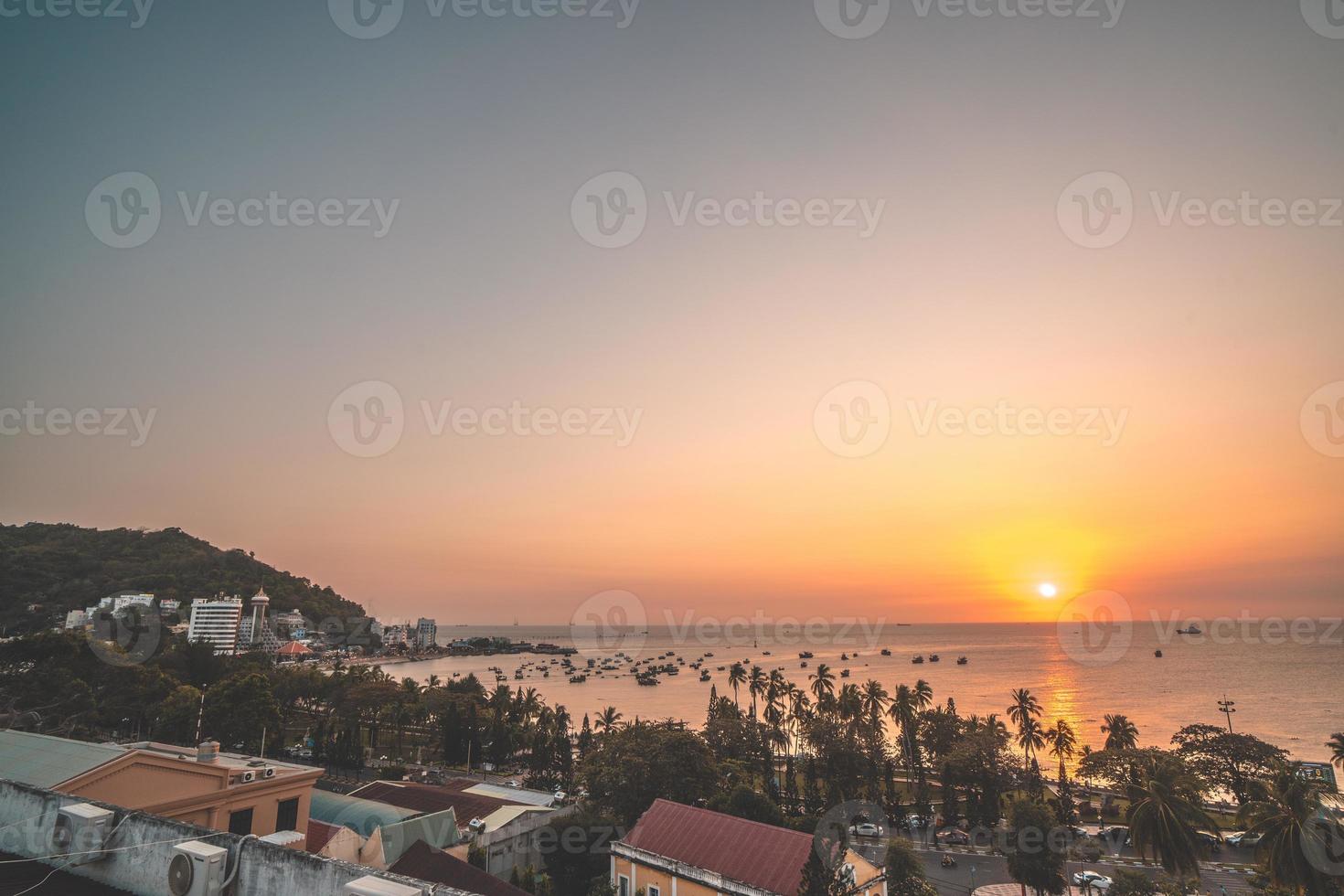 Vung Tau city aerial view with beautiful sunset and so many boats. Panoramic coastal Vung Tau view from above, with waves, coastline, streets, coconut trees and Tao Phung mountain in Vietnam. photo