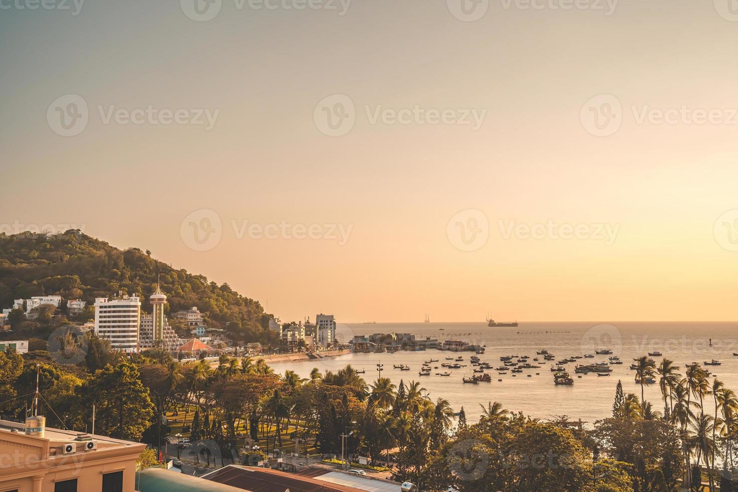 vista aérea de la ciudad de vung tau con hermosa puesta de sol y tantos barcos. vista panorámica costera de vung tau desde arriba, con olas, costa, calles, cocoteros y montaña tao phung en vietnam. foto