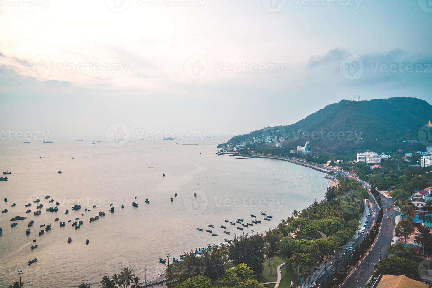 Vung Tau city aerial view with beautiful sunset and so many boats. Panoramic coastal Vung Tau view from above, with waves, coastline, streets, coconut trees and Tao Phung mountain in Vietnam. photo