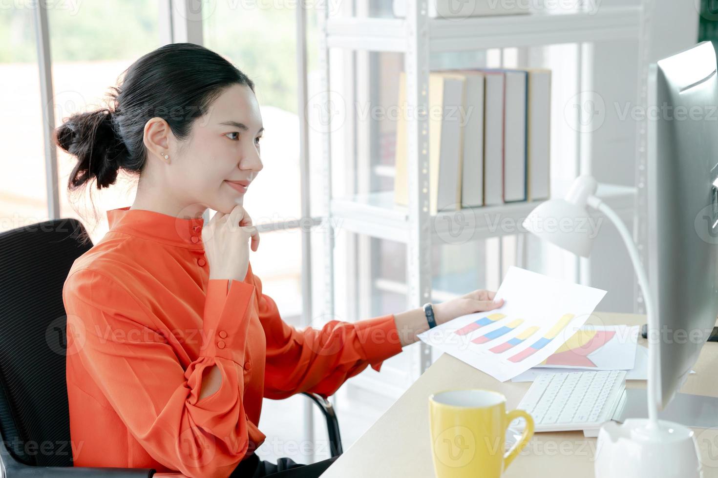 Female director working in office sitting at desk analyzing business statistics holding diagrams and charts using computer photo