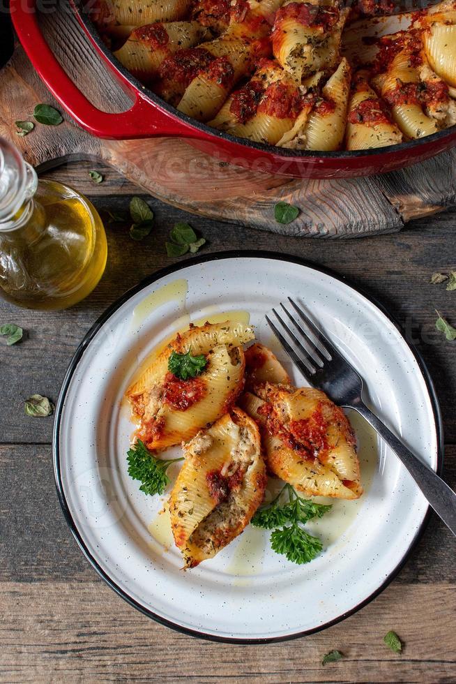 manicotti pasta shells with spinach, ricotta, mozzarella cheese in tomato sauce on plate in rustic setting flat lay photo