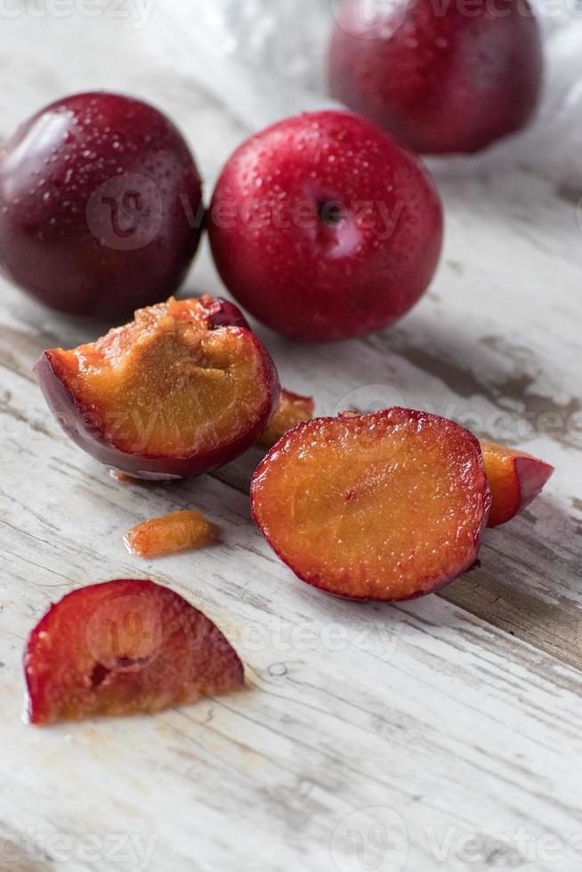 group of ripe plums sliced on white rustic table photo