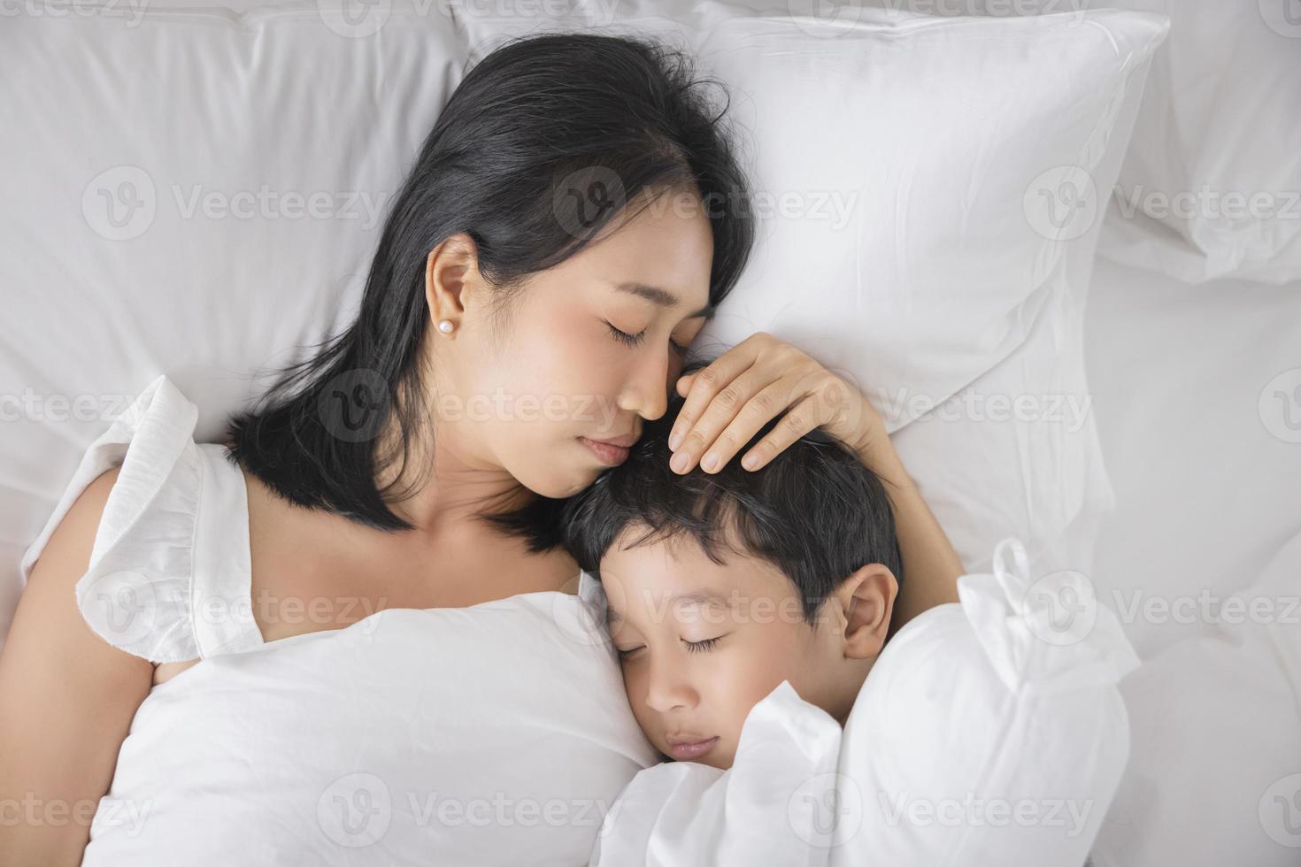 joven asiática e hijo durmiendo en su cama y relajándose en el dormitorio. están acostados de lado y se relajan con los ojos cerrados foto